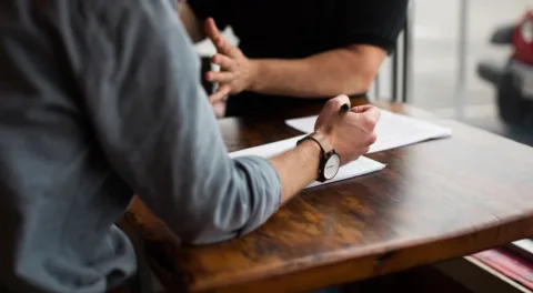 Due persone sedute allo stesso tavolo con un documento e una penna, nel momento in cui si decide se firmare