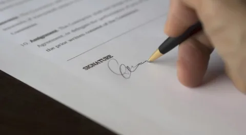 Una mano firma un modulo sulla riga della firma: la domanda è il primo passo di un contributo a fondo perduto