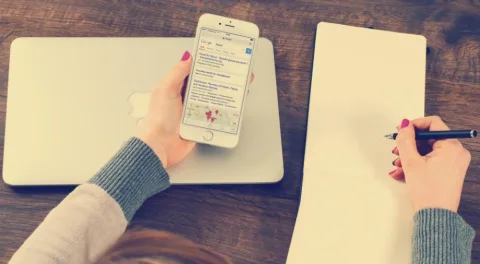 Una mano tiene il telefono con l'elenco dei messaggi, l'altra scrive su un quaderno: i contatti divisi in due posti diversi