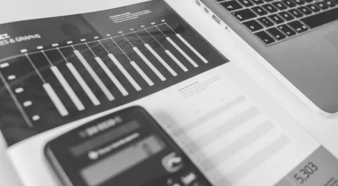 Un rapporto stampato pieno di grafici a barre appoggiato accanto a un portatile: un preventivo si legge voce per voce
