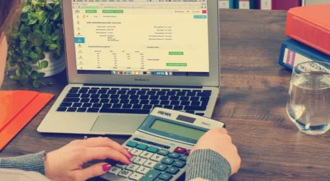 Una persona lavora al preventivo di un sito: sul portatile un foglio di conti, in mano una calcolatrice