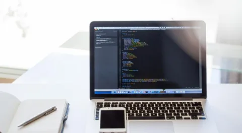 Un portatile con del codice sullo schermo, accanto un quaderno e una penna: la scelta fra un tema pronto e un sito costruito su misura